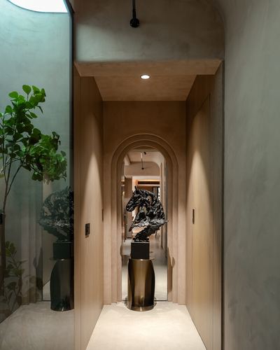 Arched corridor with wood-clad walls leading to a black horse sculpture on a brass pedestal