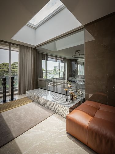 Living room with skylight, mosaic platform, leather ottoman, and marble-clad wall in Chennai apartment