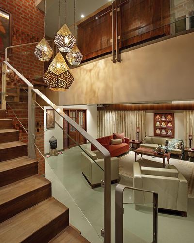 Double-height living space with exposed brick staircase, glass railings, and hanging geometric pendant lights above a seating area.