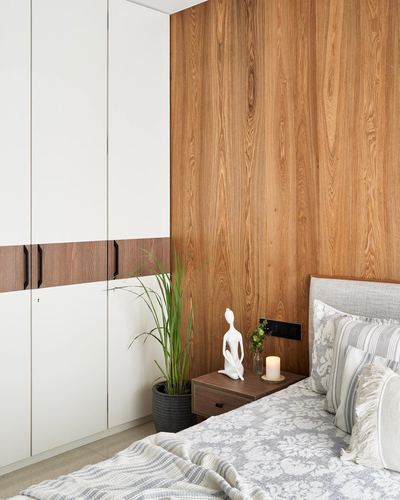 Bedroom corner with wood-paneled wall, white wardrobe, and styled nightstand beside upholstered bed