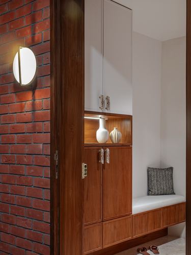Entry passage with brick wall, wooden cabinets, ceramic vases, and a cushioned bench