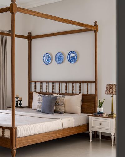 Wooden four-poster bed with blue and white plates on wall above headboard