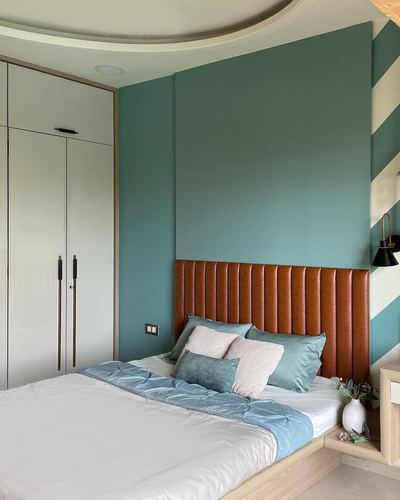 Bedroom with teal wall, tan tufted leather headboard, and diagonal striped accent wall