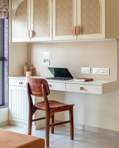 Wall-mounted study desk with cane cabinets above, wooden chair, and laptop by a window