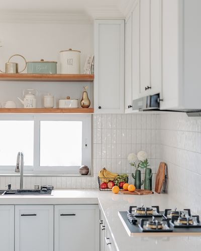 White kitchen corner with wood open shelving, tiled backsplash, and countertop fruit styling