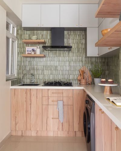 L-shaped kitchen with sage ribbed tile backsplash, wood cabinetry, black chimney hood and hob