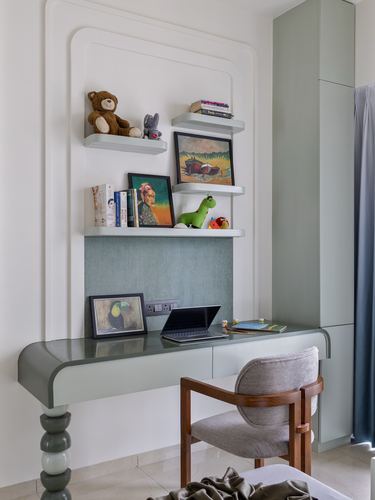 Sage green built-in desk with floating shelves of books and art in a niche
