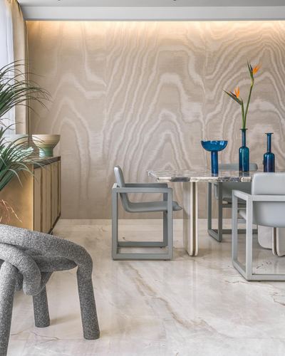 Dining area with marble table, grey chairs, knotted bench, and blue glass vases against wavy textured wall