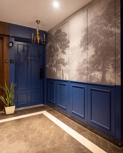 Entry vestibule with blue panelled door, brass chandelier, and forest mural wallpaper over marble floor