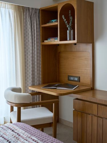 Walnut veneer fold-down desk nook with arched shelf niche and cream boucle chair by a curtained window