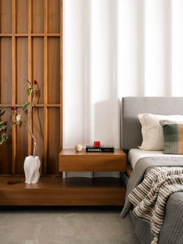Floating wood nightstand with books and vase beside upholstered bed and wooden lattice wall