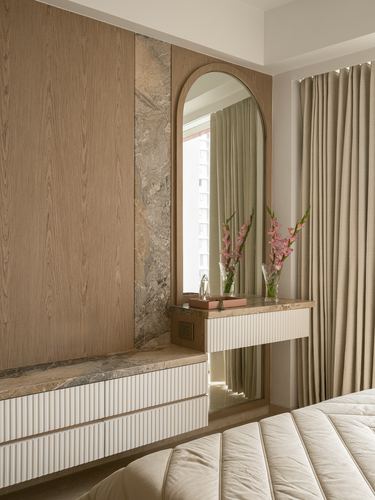 Arched mirror above fluted white dresser with stone counter beside curtained window in bedroom