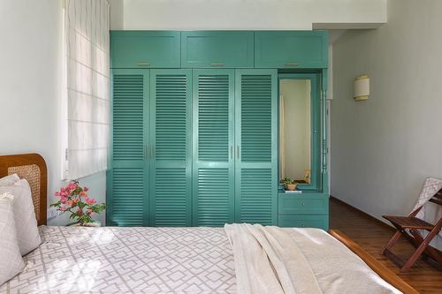 Bedroom with teal louvered wardrobe, cane headboard bed, and mirrored dressing nook.