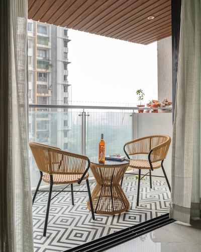 Balcony with two rattan chairs, hourglass side table, patterned floor tile, and city view