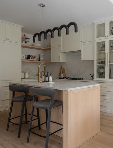 Cream kitchen with light wood island, black tubular pendant, and brass fixtures