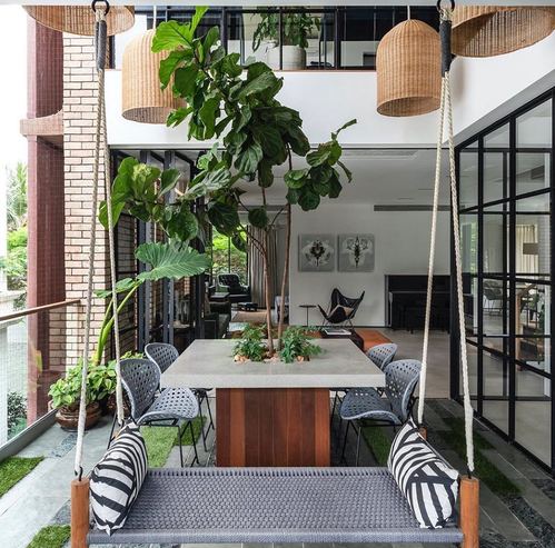 Double-height courtyard balcony with hanging swing, tree through dining table, and rattan pendants