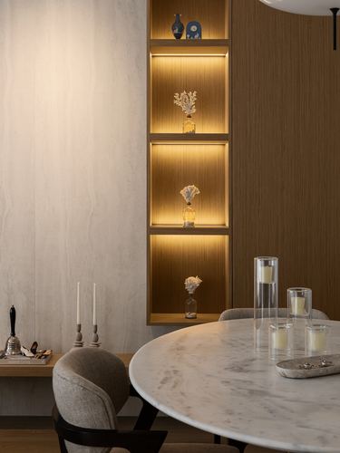 Dining nook with marble table, candles, and a backlit wooden display niche with decorative objects