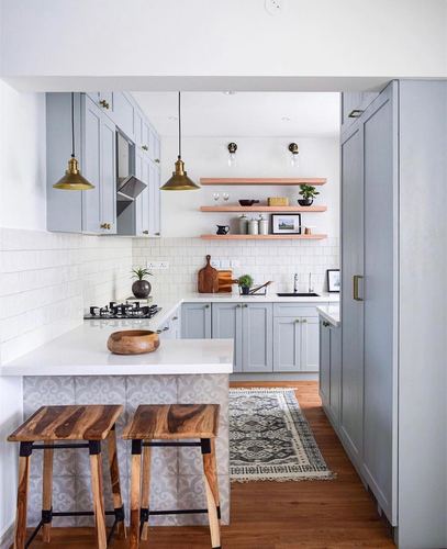 Grey and white galley kitchen with brass pendant lights, wood bar stools, and open shelving