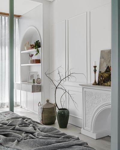 White paneled bedroom wall with arched shelving niche, marble console, and decorative fireplace with branches in a vase