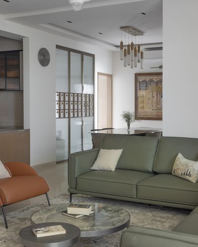 Living room with sage green leather sofa, round marble coffee tables, and terracotta accent chair, dining area glimpsed through frosted glass partition
