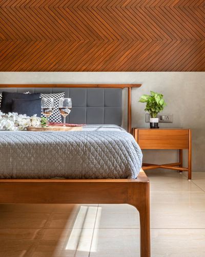Bedroom with grey tufted headboard, wooden bed frame, chevron wood ceiling and bedside table with plant