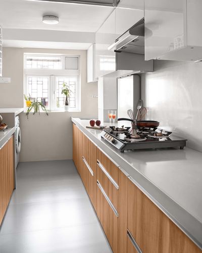 Narrow galley kitchen with wood-toned cabinetry, white overhead units, and a gas hob under a window at the far end.