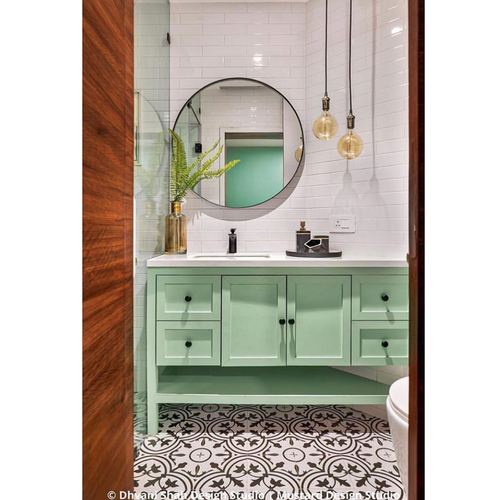 Bathroom with mint green vanity, round mirror, subway tile walls and patterned floor, seen through wooden door
