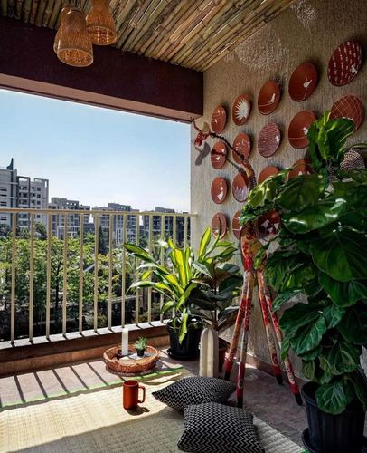 Balcony with bamboo ceiling, terracotta plate wall art, plants and floor cushions overlooking city