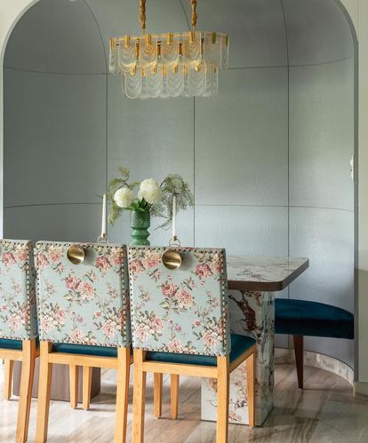 Dining nook in arched alcove with floral chairs, marble table, and layered chandelier