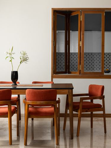 Dining table with orange upholstered wooden chairs beside a tiled internal window