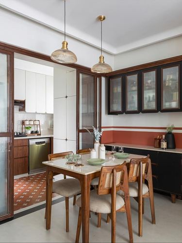 Dining area with cane chairs, marble-top table, brass pendants, and terracotta accent wall opening to kitchen