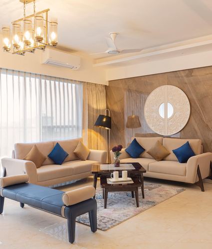 Beige living room with two sofas, blue cushions, round carved mirror on stone wall