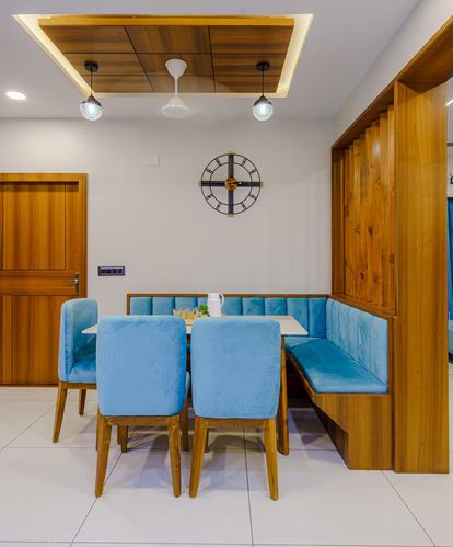 Blue velvet dining chairs and corner banquette under a wood-panelled ceiling with pendant lights
