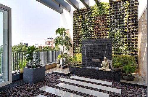Terrace with black stone water feature, buddha statue, pebble floor and vertical green wall