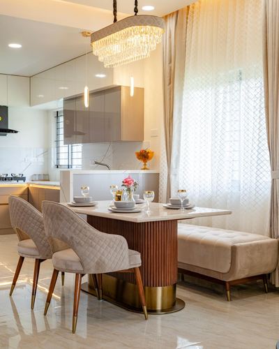 Dining table with fluted brass base, tufted bench, and crystal chandelier beside kitchen