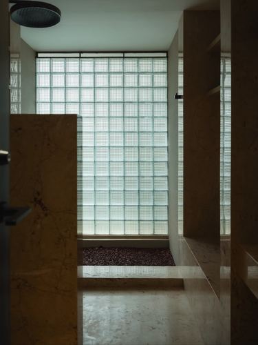 Bathroom framed by stone walls with a glass block window glowing behind a pebble floor inset