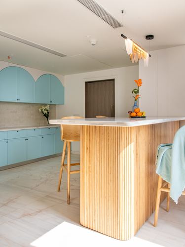 Coastal-style kitchen with blue arched cabinets and a fluted wood island under a sculptural pendant light