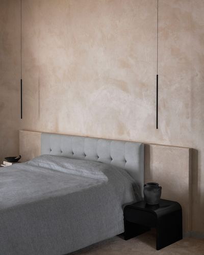 Bedroom with tufted grey headboard, black nightstand and vase against warm plaster wall with pendant lights