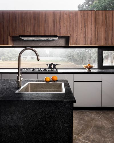 Kitchen island with black stone counter, sink, and gas hob, walnut cabinetry above, garden view through window strip