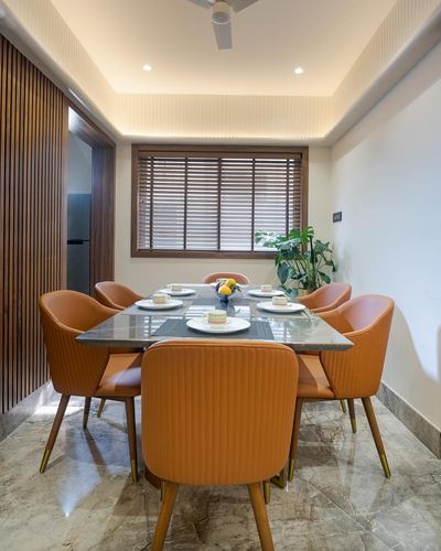 Dining room with orange velvet chairs, marble-top table, wooden blinds and fluted panelling