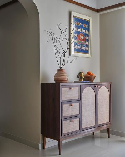 Wooden cane-front console with vase, brass bust and framed painting in an arched foyer niche