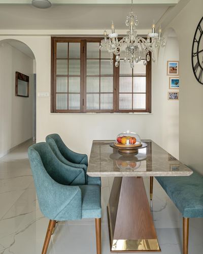 Dining nook with marble table, teal upholstered chairs, crystal chandelier and wood-framed window