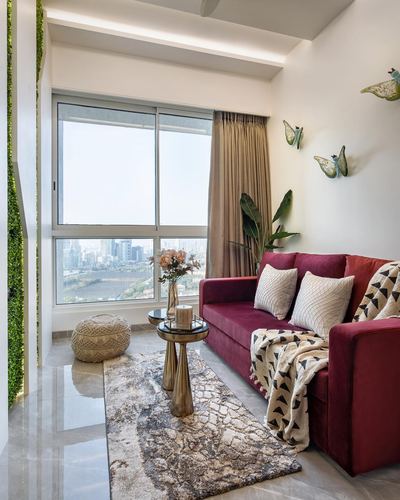 Maroon velvet sofa by a large window overlooking Mumbai skyline, patterned rug and brass table
