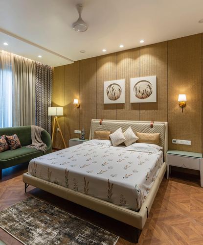 Bedroom with beige upholstered bed against a textured gold wall panel, flanked by sconces and circular artwork, green sofa to the side.