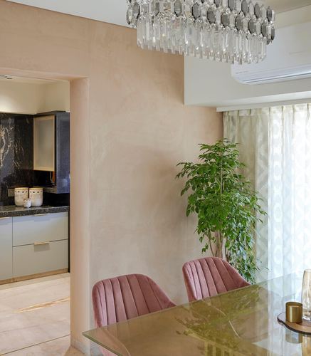Dining nook with pink velvet chairs, glass table, crystal chandelier, and view into kitchen with sage cabinetry