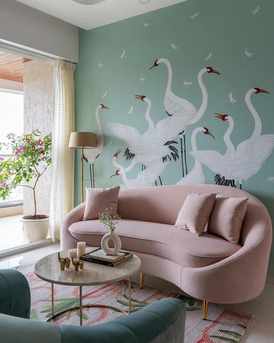Pink curved sofa before a sage green wall painted with white swans