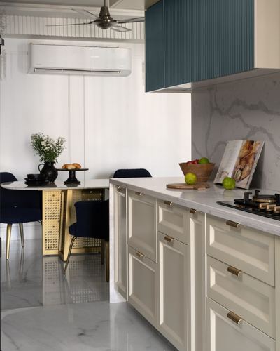Cream kitchen with marble countertop and teal fluted cabinet, dining table with navy cane chairs beyond