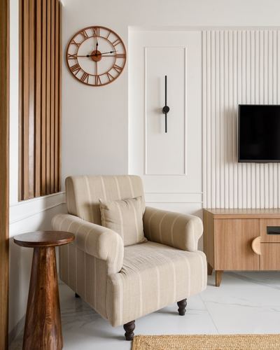 Beige striped armchair beside carved wood side table under a large wooden wall clock