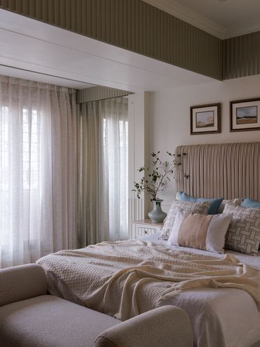 Bedroom with pleated headboard, sheer curtains, and green fabric-clad ceiling detail above bed