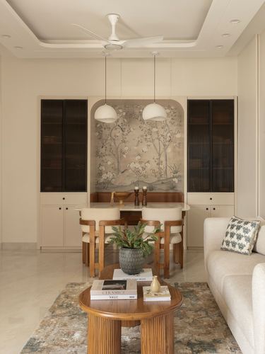 Neutral dining nook with botanical mural, dome pendants, wooden table and cane chairs, coffee table with books in foreground